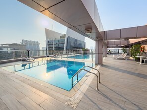 A rooftop pool with clear glass railings, lounge chairs, and a view of the cityscape. - Stayshort - Elegant 2 Bedroom That Sleeps 4 (Dubai)