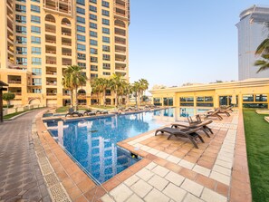 Ein Hotelpoolbereich mit Liegestühlen, einem Schwimmbecken und einem Hochhaus im Hintergrund.