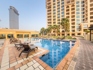 Ein Hotelpoolbereich mit Liegestühlen und einem großen Gebäude im Hintergrund.