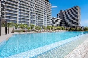 Ein Swimmingpool mit Liegestühlen und einem modernen Gebäudekomplex im Hintergrund.