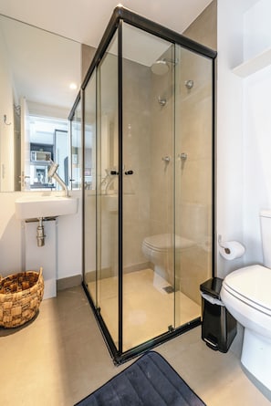 A modern bathroom with a glass-enclosed shower, a toilet, and a sink with a mirror above it. - Vrbo Property (São Paulo)
