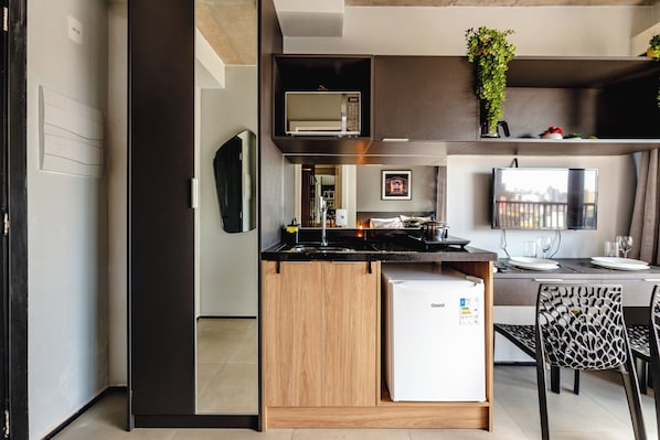 A compact kitchen with a built-in refrigerator, a microwave, and a sink. - Vrbo Property (São Paulo)