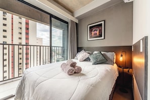 A hotel room with a large bed, a framed picture on the wall, and a view of the cityscape through the window. - Vrbo Property (São Paulo)