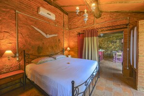 A bedroom with a bed, bedside lamps, a stone wall, and a view of an outdoor area. - Chale completo , todo murado,a 200mts da praia, pet-friendly (Ilhabela)