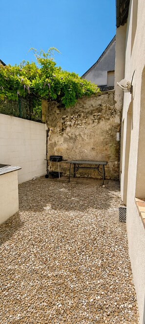 Un pati amb sòl de grava, una banca, una barbacoa i una paret coberta de plantes enfilades.