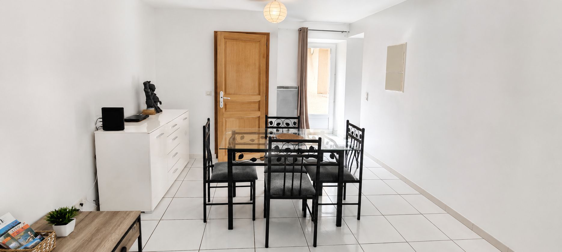Een kleine keuken met een eettafel en stoelen, een witte koelkast en een houten deur.
