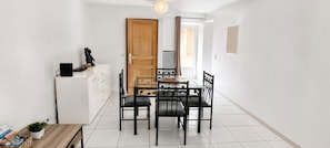 Een kleine keuken met een eettafel en stoelen, een witte koelkast en een houten deur.