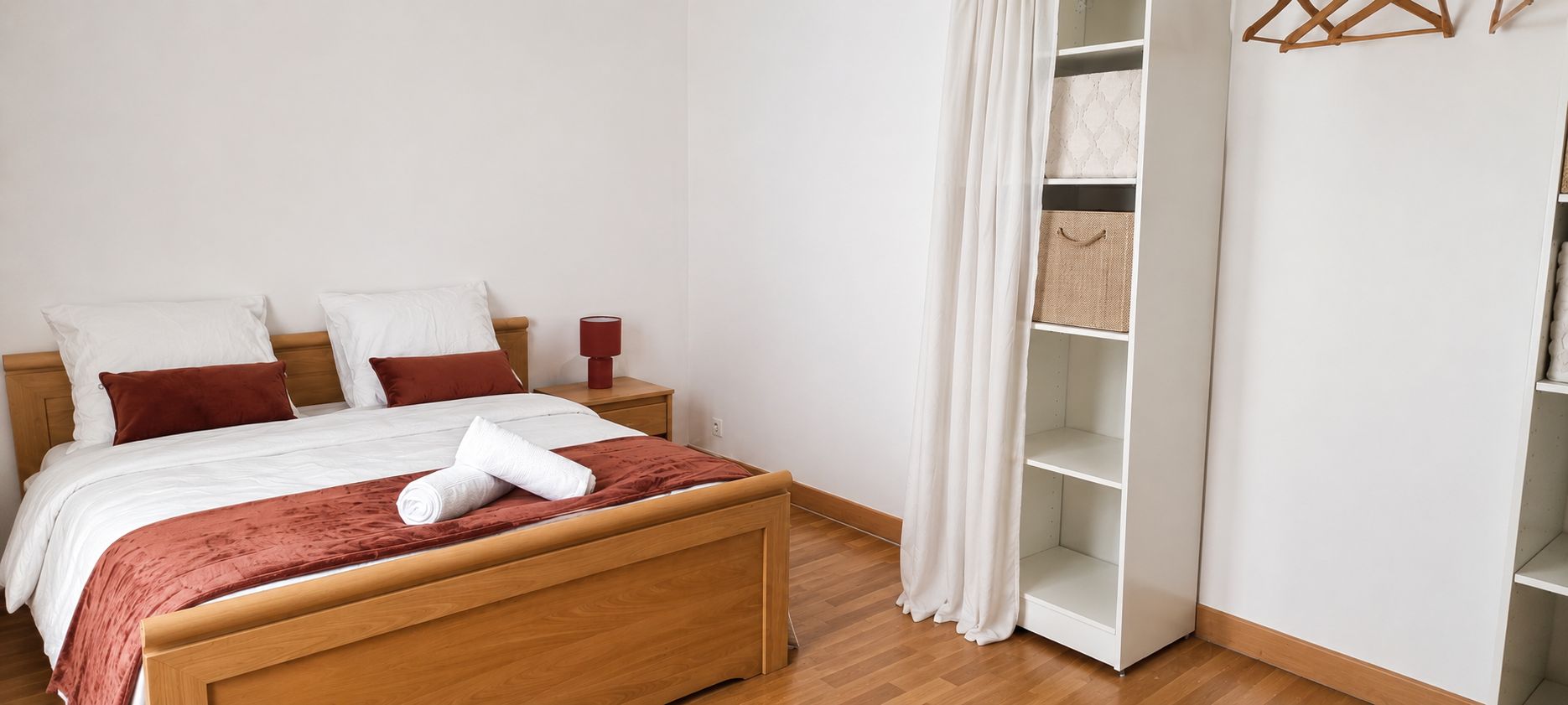 Een netjes opgemaakt bed met een houten hoofdbord, een rode plaid en een wit kussen.