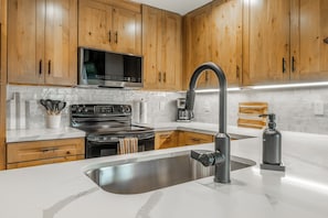 A modern kitchen with wooden cabinets, a stainless steel sink, a black faucet, a microwave, and a stove. - Just Renovated & Steps to Village! 2BR/2BA + Loft (Mammoth Lakes)