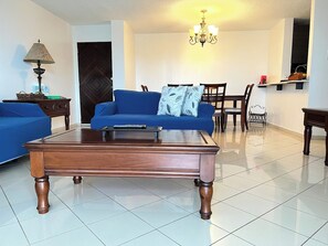 A living room with a wooden coffee table, blue sofas, a dining table with chairs, and a chandelier. - Beautiful La Mancha Apartment + free parking (Carolina)