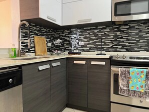 Una cocina moderna con armarios oscuros, un microondas de acero inoxidable y un salpicadero de azulejos.