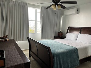 A hotel room with a bed, a desk, a chair, a ceiling fan, and a window with curtains. - Beautiful La Mancha Apartment + free parking (Carolina)