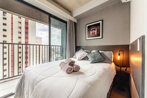 Een hotelkamer met een groot bed, een ingelijst kunstwerk aan de muur en een uitzicht op de stadsgezichten door het raam.