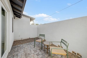Eine Terrasse mit zwei Stühlen, einem Tisch, einer weißen Wand und einem wolkenlosen Himmel.