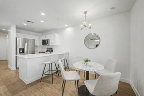 Una cocina moderna con muebles blancos, un refrigerador de acero inoxidable y un microondas. Hay un comedor con una mesa redonda y cuatro sillas.