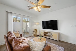 A modern living room with a leather sofa, a round coffee table, a TV on the wall, and a ceiling fan. - Warm 2BR Phoenix Home | Private Patio + Parking (Phoenix)