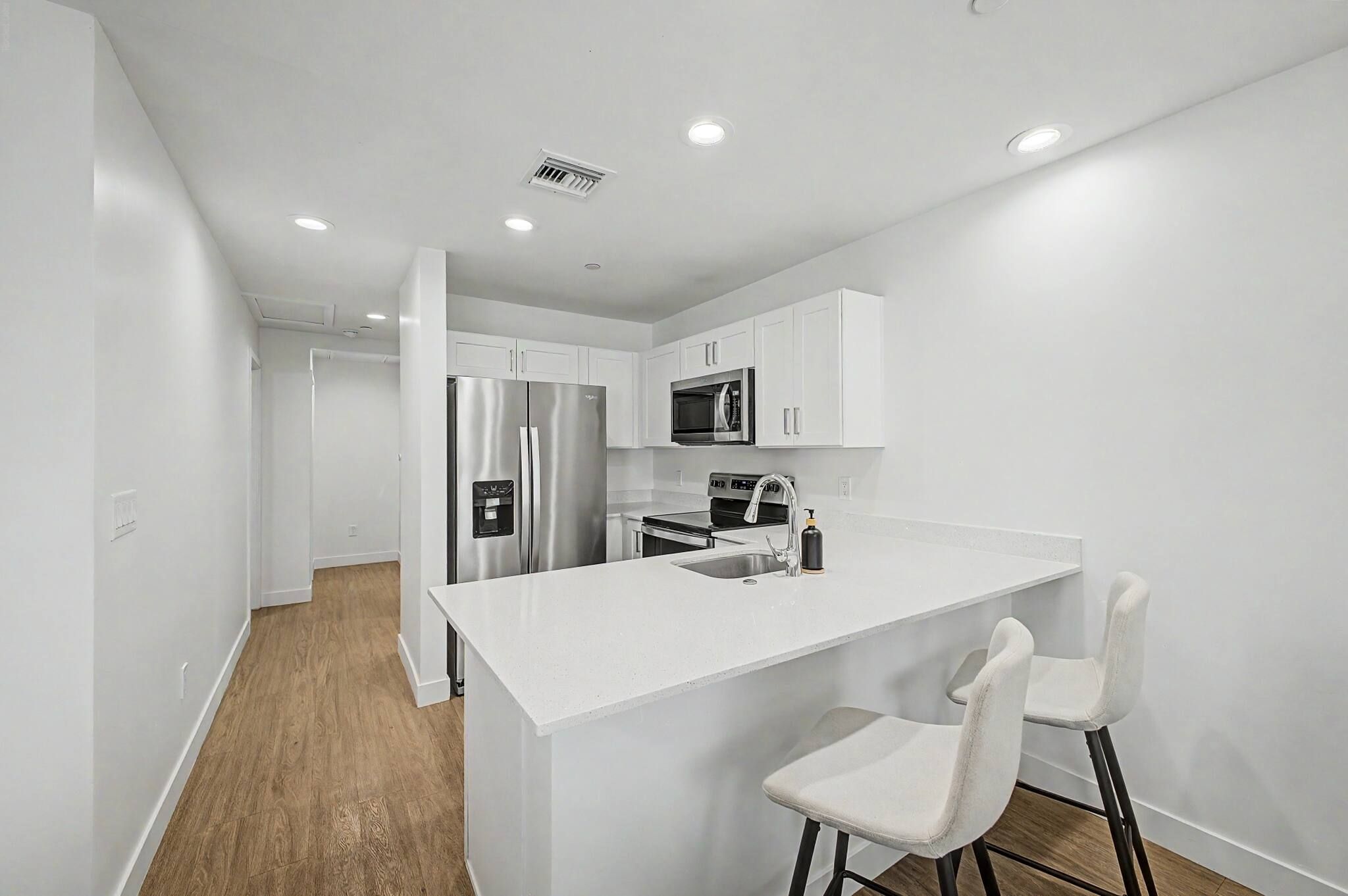 A modern kitchen with white cabinetry, stainless steel appliances, and a central island with bar stools.