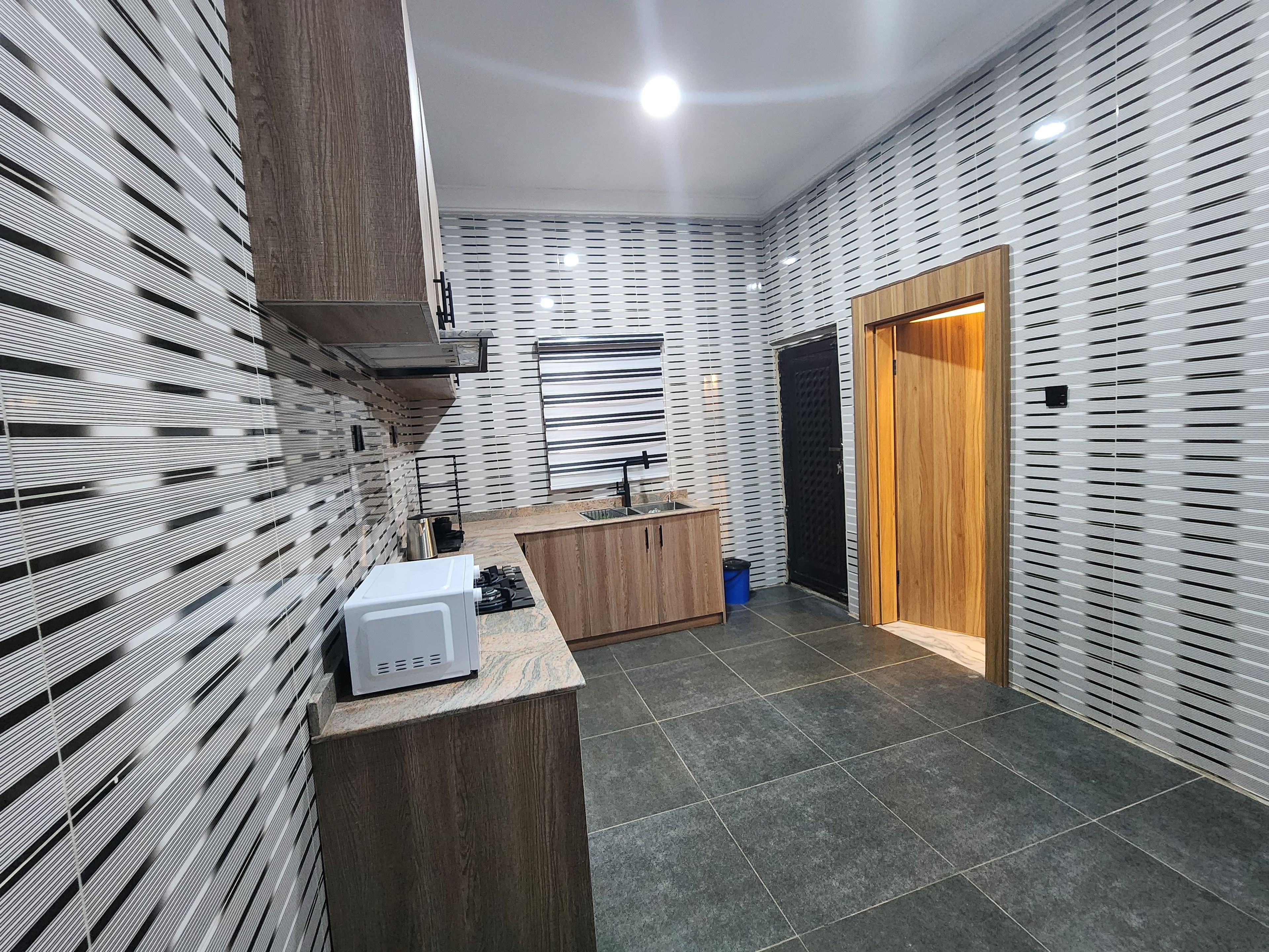 A modern kitchen with a built-in microwave, wooden cabinets, and a black door.