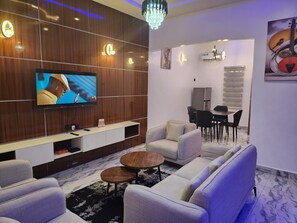 A modern living room with a flat-screen TV, sofas, a dining area, and decorative wall art.