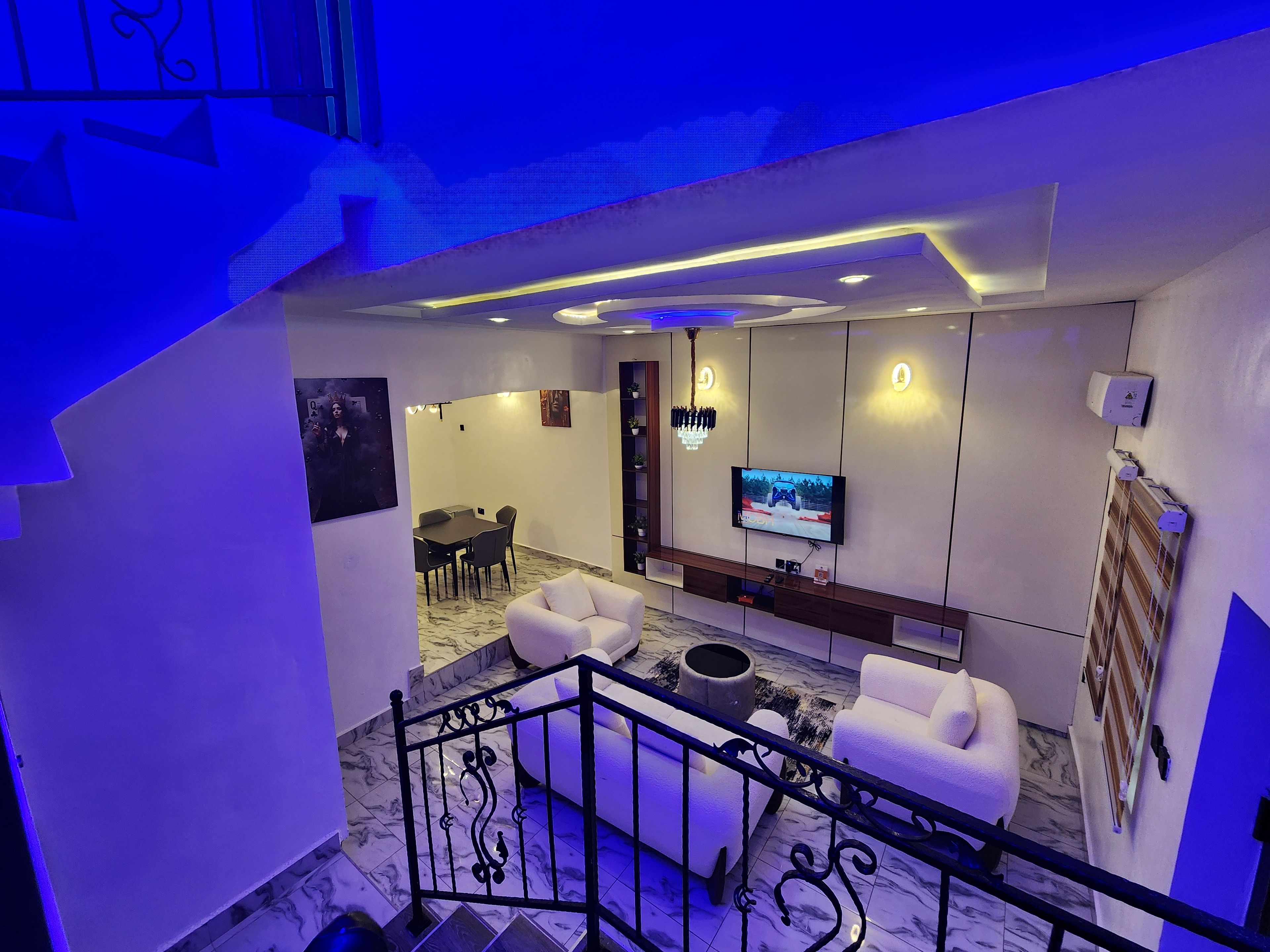 Un salon moderne doté d’un téléviseur à écran plat, de canapés blancs, d’un coin repas et d’un escalier.
