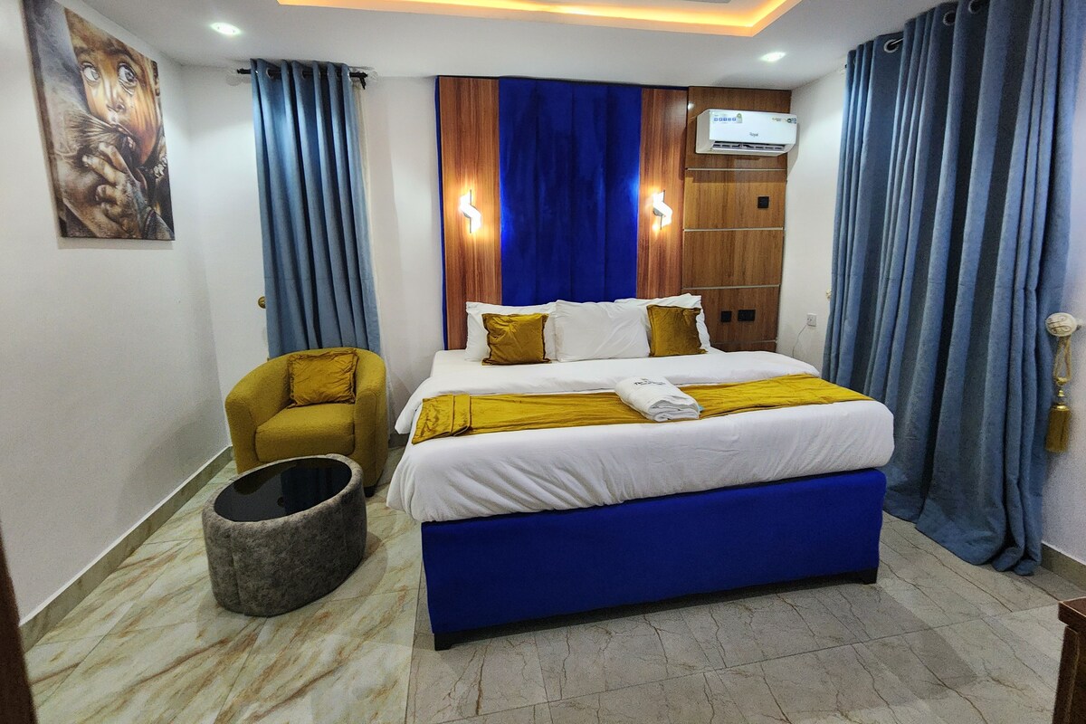 A hotel room with a bed, a chair, a wall-mounted TV, and a wooden wardrobe.