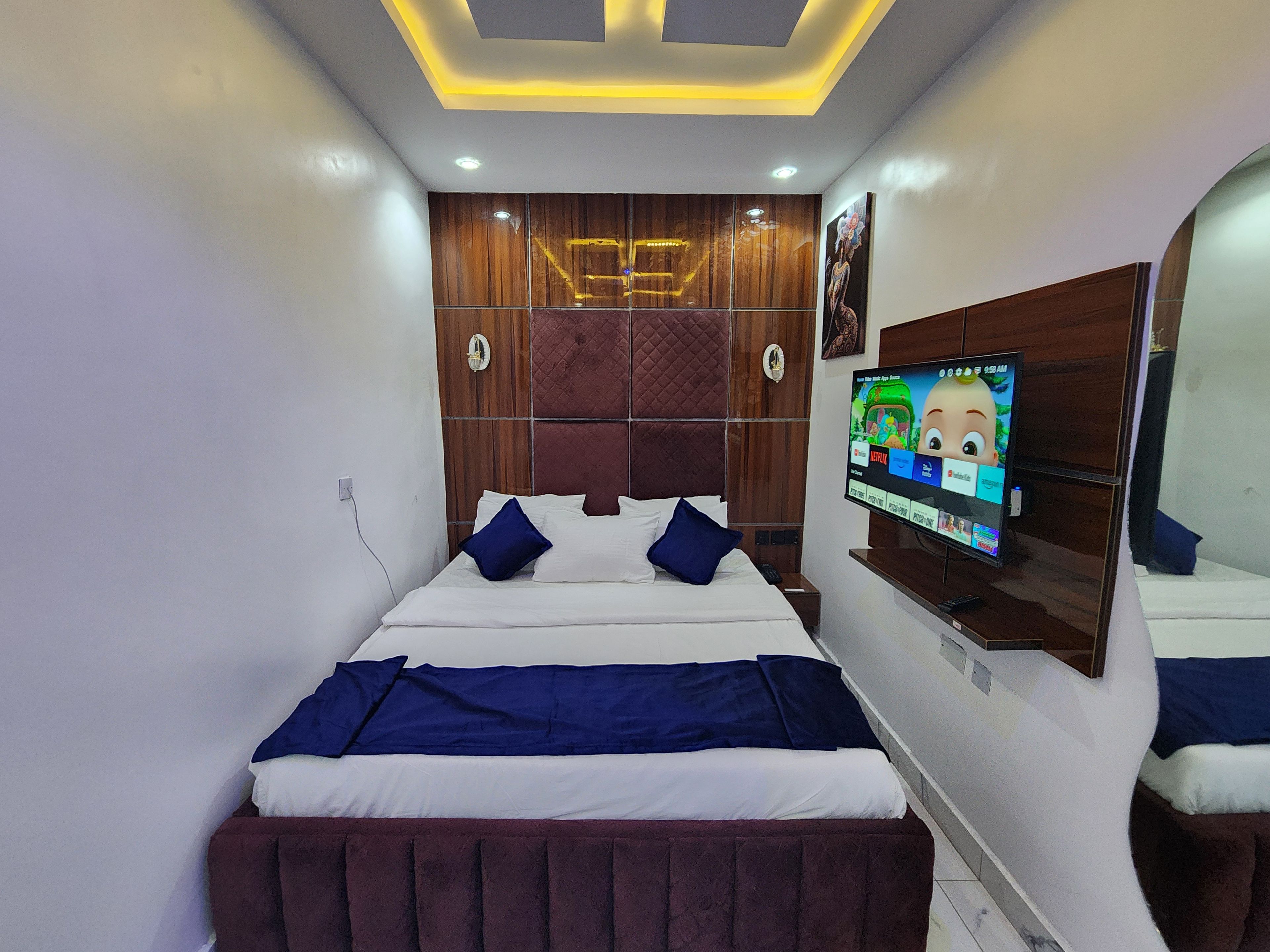 A modern bedroom with a bed, a television mounted on the wall, and a wooden headboard.