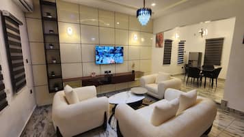 Uma sala de estar moderna com televisão de tela plana, sofás confortáveis, uma mesa de centro e uma área de jantar com cadeiras e uma mesa.