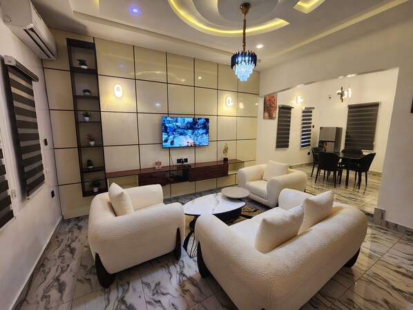 Una sala de estar moderna con un televisor de pantalla plana, sofás cómodos, una mesa de centro y un comedor con sillas y una mesa.