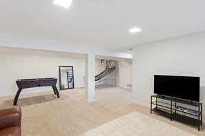 A room with a foosball table, a television on a stand, and a staircase in the background. - Pet Friendly Game Room Westside Retreat Near Garden of Gods Walk 3blks to OCC (Colorado Springs)