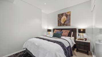 A bedroom with a bed, bedside lamps, a nightstand, and a wall-mounted artwork.