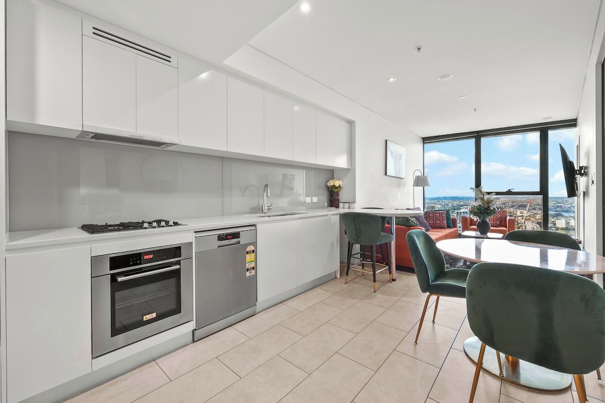 A modern kitchen with built-in appliances, a dining area with a round table and chairs, and a large window offering a city view.
