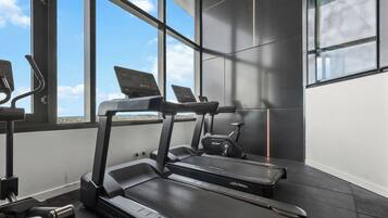 A modern gym with treadmills and exercise equipment, large windows, and a view of the sky.