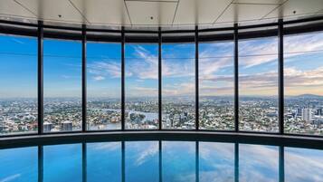 A panoramic view from a high-rise building with a glass floor, overlooking a cityscape with buildings and a river.