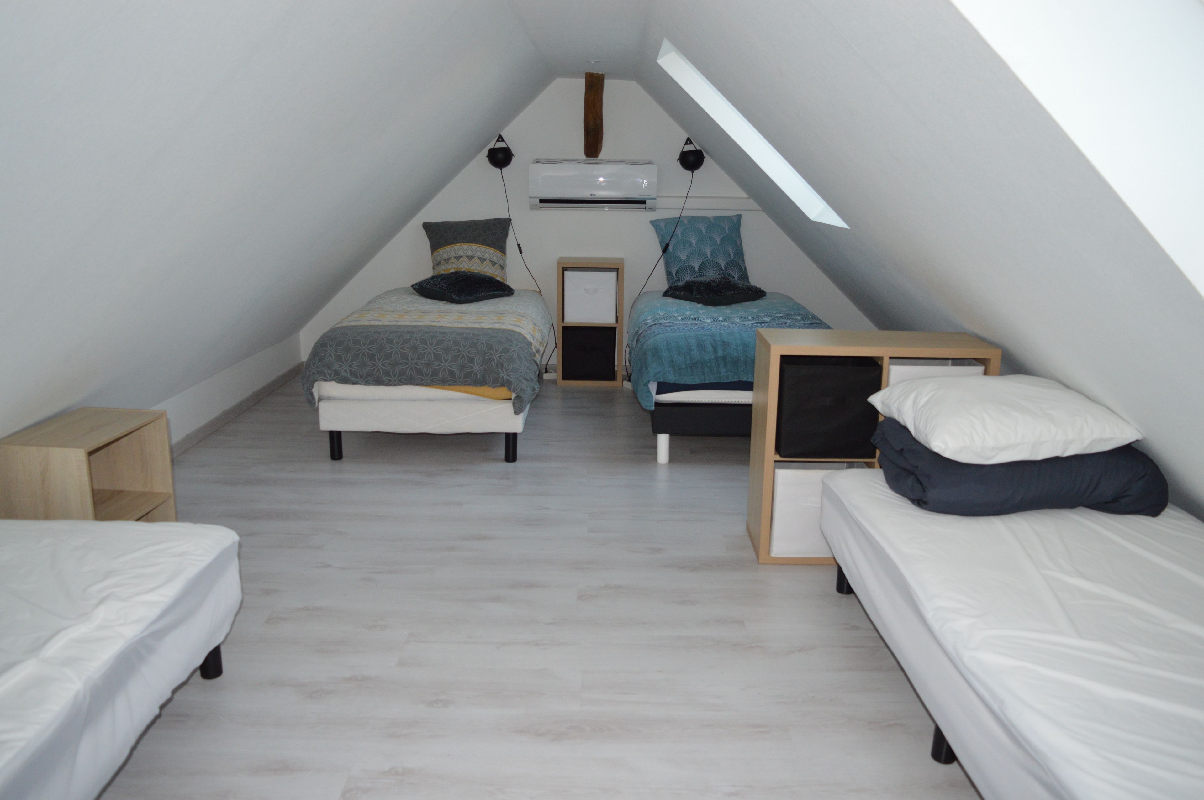 Een knus, driekantig slaapkamer op zolder met twee bedden, een houten nachtkastje en een plafondventilator.