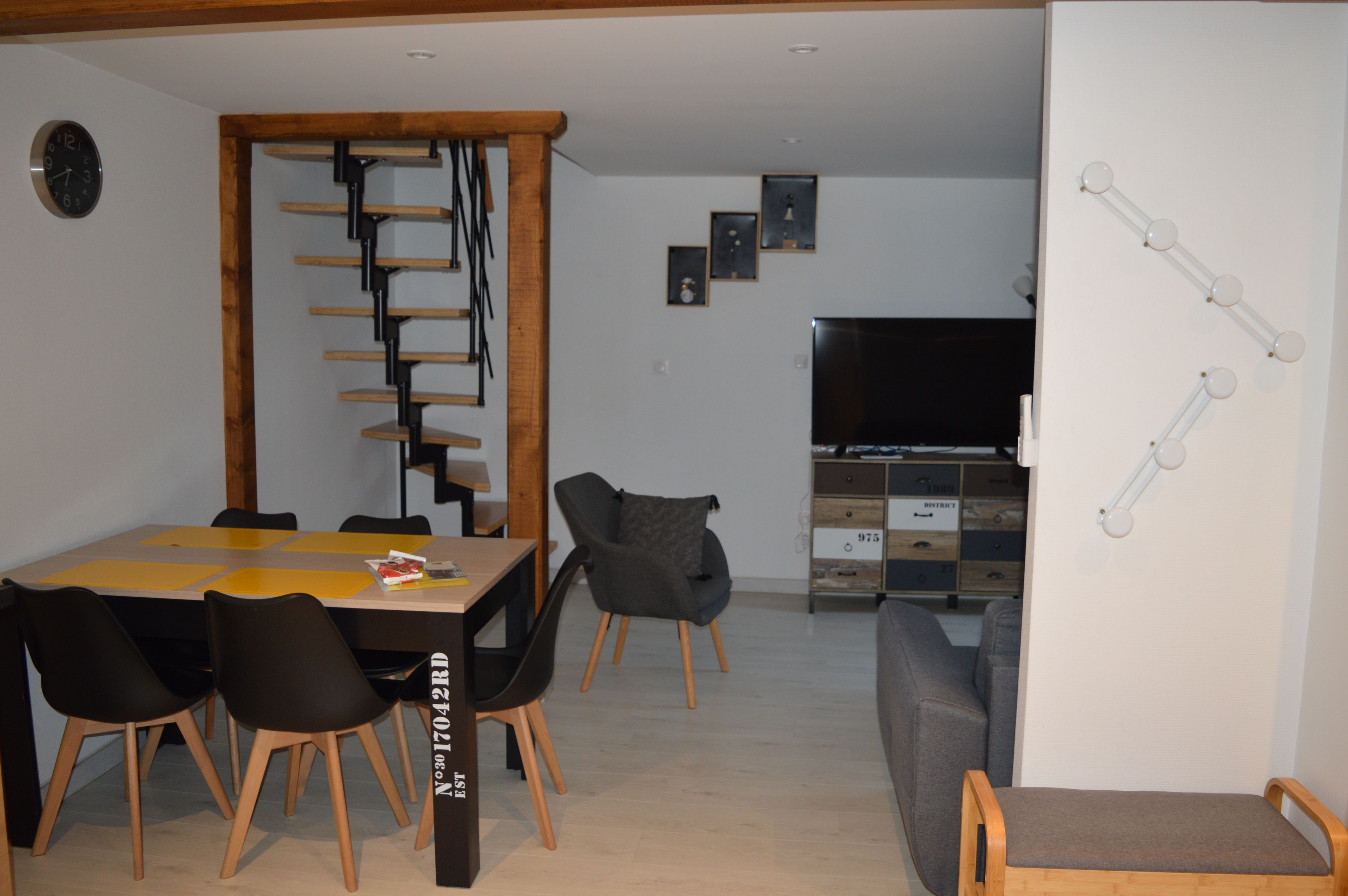 En matplats med ett träbord och stolar, en trappa, en tv och en väggmonterad lampa.