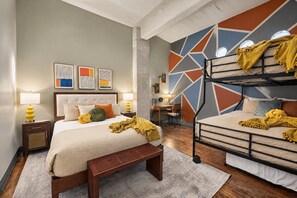 A bedroom with a bunk bed, a bed with a headboard, bedside tables with lamps, and artwork on the wall. - The Bentley Collection - The Marquee (Dallas)