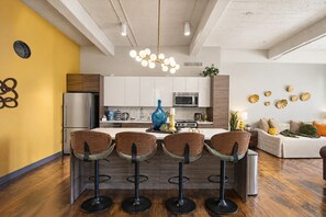 A modern kitchen with a central island, bar stools, and a dining area with a sofa. - The Bentley Collection - The Marquee (Dallas)