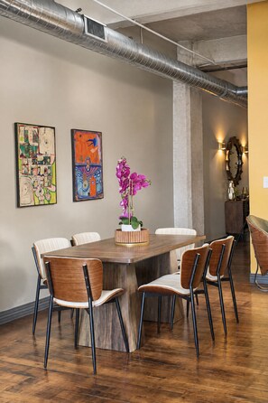 A conference room with a wooden table, six chairs, two abstract paintings, a potted orchid, and exposed ductwork on the ceiling. - The Bentley Collection - The Marquee (Dallas)