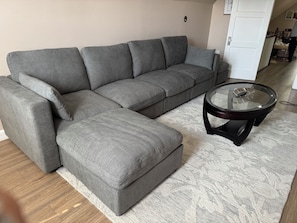 Ein graues Ecksofa mit einem Glastisch in einem Zimmer mit einem gemusterten Teppich.