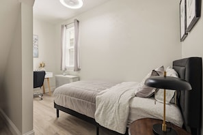 Ein Schlafzimmer mit Bett, Nachttisch, Lampe und Schreibtisch mit Stuhl.