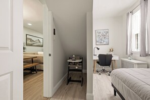 Een slaapkamer met een bed, bureau en stoel. Op de muur hangt een schilderij en er is een raam met gordijnen.