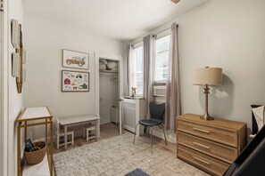 Ein Kinderzimmer mit einem Babybett, einem kleinen Tisch, einem Stuhl, einer Kommode und einer Lampe.