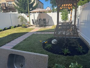 Een achtertuin met terras, tuinmeubilair, een pergola en een tuin met een kleine vijver.