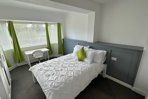 Een hotelkamer met een bed, een bureau en een raam met gordijnen.
