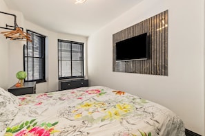 A bedroom with a bed, two windows with blinds, a wall-mounted TV, and a hanging light fixture. - 1 Bedford House - Close to Town and Seafront (Tenby)