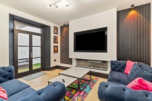 A modern living room with a flat-screen TV, dark sofas, a coffee table, and a fireplace. - 1 Bedford House - Close to Town and Seafront (Tenby)