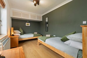Ein Zimmer mit zwei Holzbettställen, einem kleinen Schreibtisch mit Lampe, einem Heizkörper und einem gerahmten Bild an der Wand.