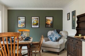 Ein Essbereich mit einem Holztisch und Stühlen, einer Couch und einem Schrank. An der Wand hängen drei gerahmte Bilder.