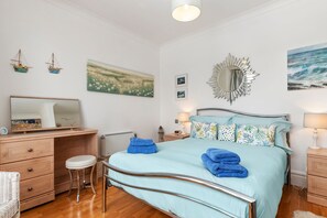 Ein Schlafzimmer mit Bett, Nachttischen, einem Schreibtisch, einem Stuhl und Kunstwerken an den Wänden.