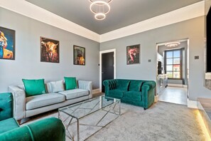 Ein modernes Wohnzimmer mit einem grauen Sofa, einem grünen Samtsofa und einem Glastisch.
